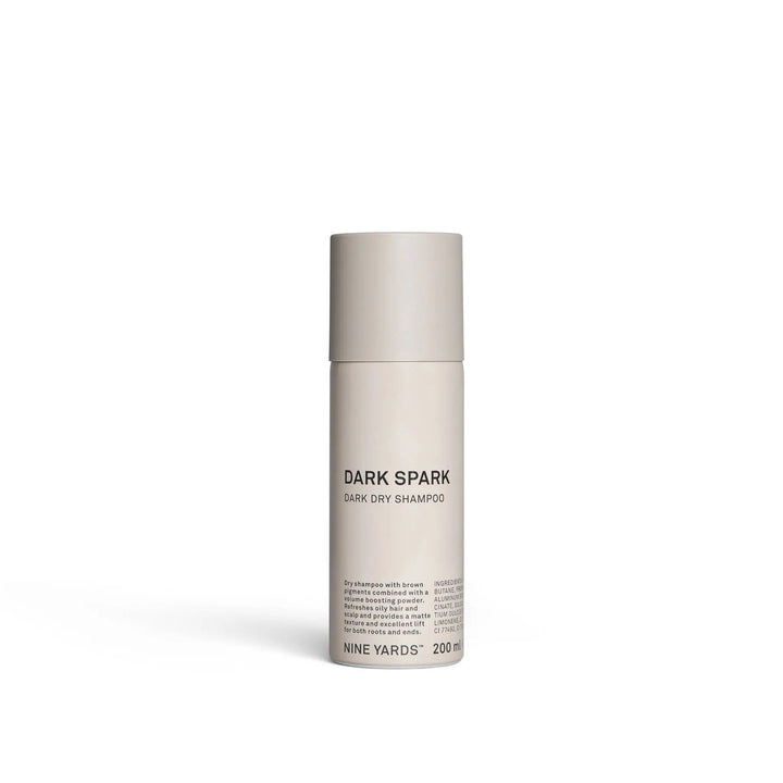 Smėlio spalvos cilindrinis buteliukas NINE YARDS Dark Spark Dark Dry Shampoo 200ml, paprastas minimalistinis dizainas ir derantis smėlio spalvos dangtelis. Produktas stovi baltame fone.